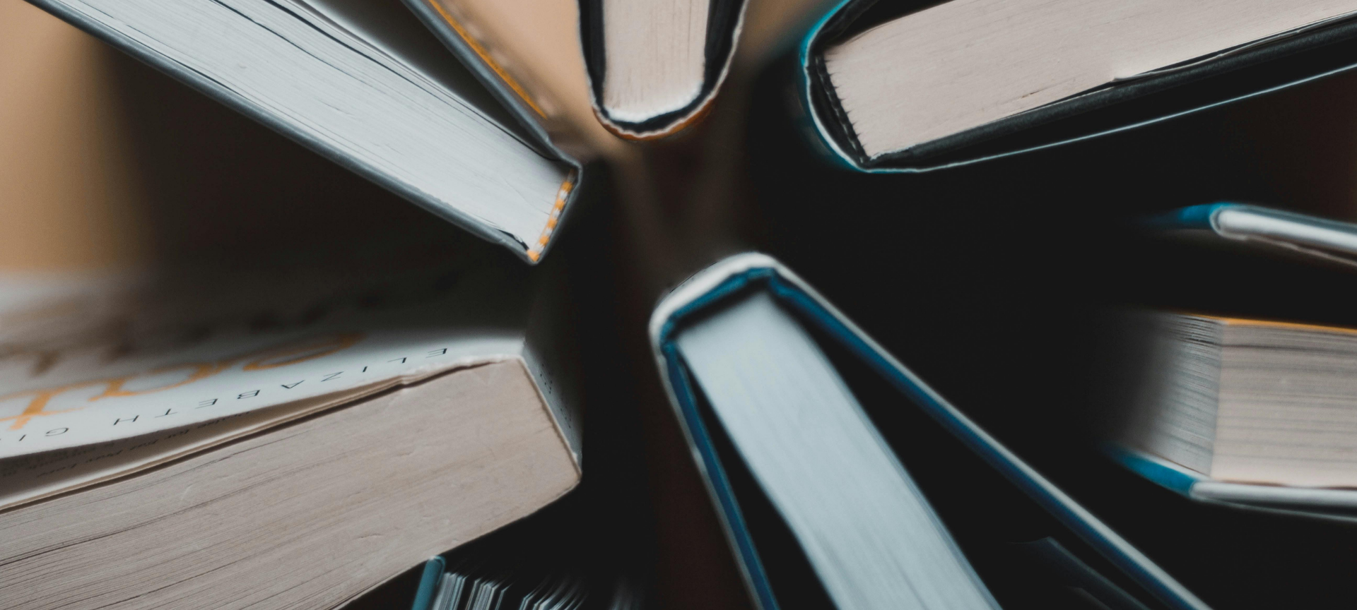 Mehrere geschlossene Bücher liegen kreisförmig mit ihren Schnittkanten nach innen, sodass eine sternförmige Öffnung entsteht. Die Aufnahme ist sehr nah und erzeugt einen starken Perspektiveffekt.