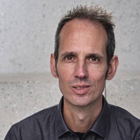 Jens Jacobsen hat kurzes, dunkles Haar. Er trägt ein dunkles Hemd.