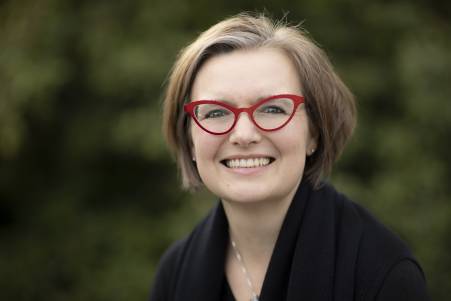 Katja Busch hat kurzes, dunkelblondes Haar. Sie trägt eine rote Brille und lächelt.